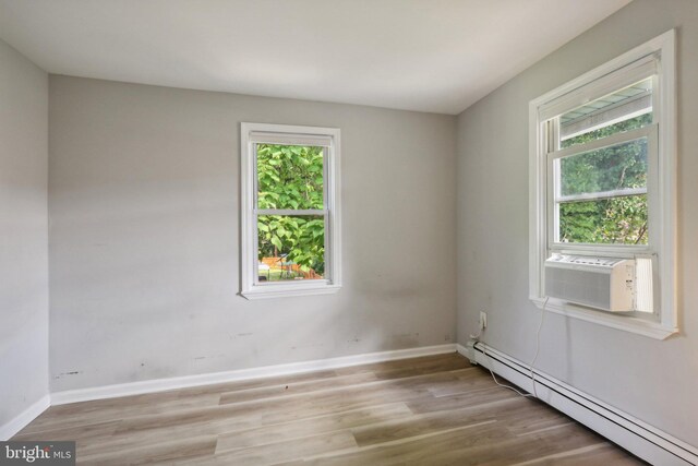 empty room with a baseboard heating unit, hardwood / wood-style floors, and cooling unit