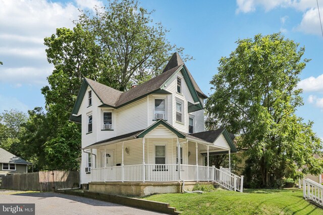 victorian-style house featuring a porch, cooling unit, and a front yard