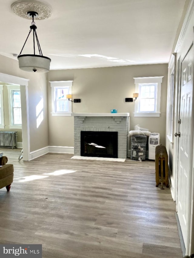 unfurnished living room with radiator, wood-type flooring, and a brick fireplace