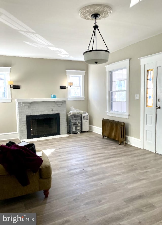 living room with radiator heating unit, hardwood / wood-style flooring, plenty of natural light, and a brick fireplace