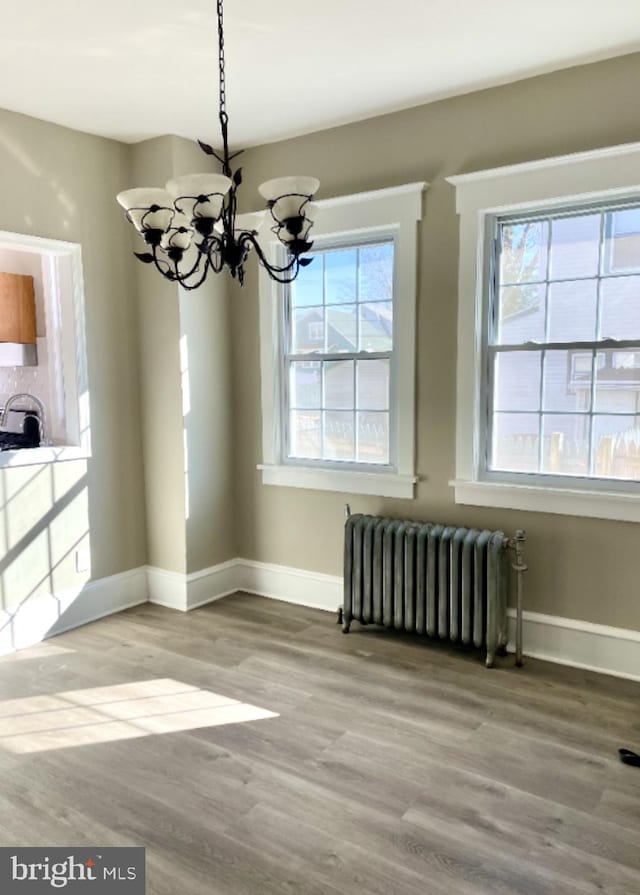 unfurnished dining area featuring radiator heating unit, wood-type flooring, and an inviting chandelier