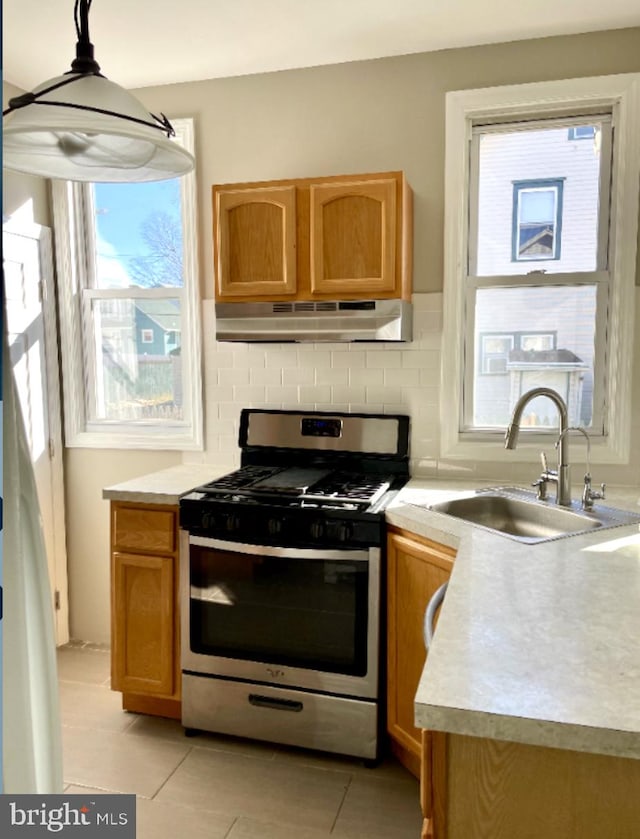 kitchen featuring sink, light tile patterned floors, stainless steel gas stove, and a healthy amount of sunlight