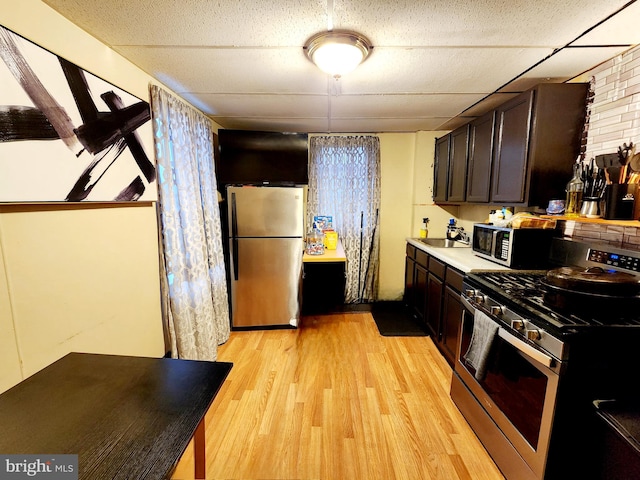 kitchen featuring light wood-type flooring, stainless steel appliances, brick wall, dark brown cabinetry, and sink