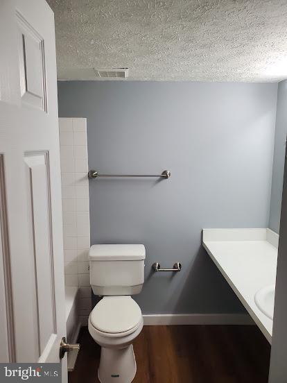 bathroom with toilet, a textured ceiling, vanity, a bath, and hardwood / wood-style flooring