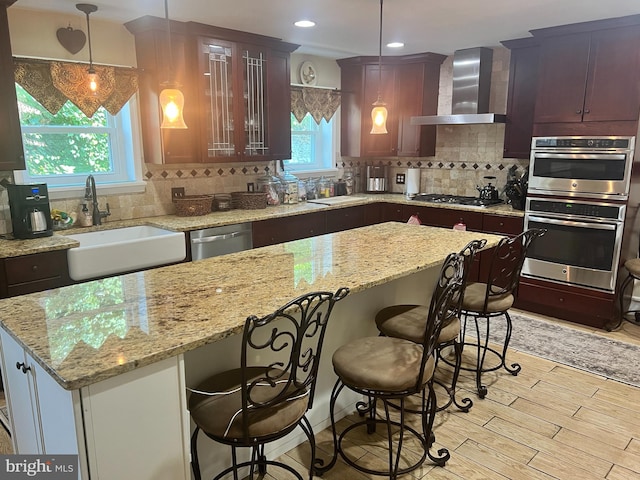 kitchen with appliances with stainless steel finishes, wall chimney range hood, decorative backsplash, and decorative light fixtures