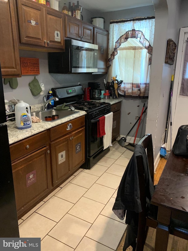 kitchen featuring light tile patterned flooring, sink, gas range oven, and dark brown cabinetry