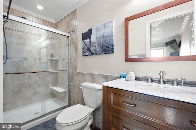 bathroom featuring a shower with door, tile walls, vanity, ornamental molding, and toilet