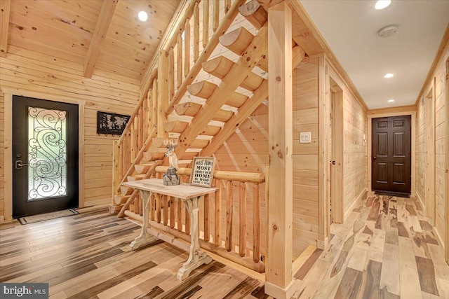 entryway featuring wood walls, light hardwood / wood-style flooring, and vaulted ceiling with beams