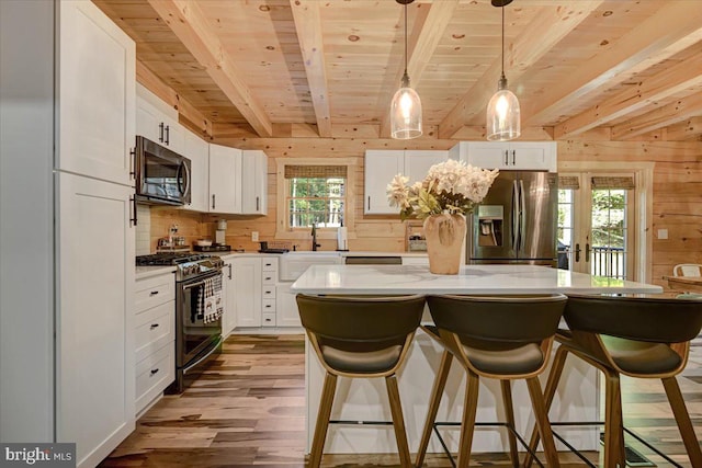 kitchen with white cabinets, a kitchen island, light hardwood / wood-style floors, appliances with stainless steel finishes, and pendant lighting