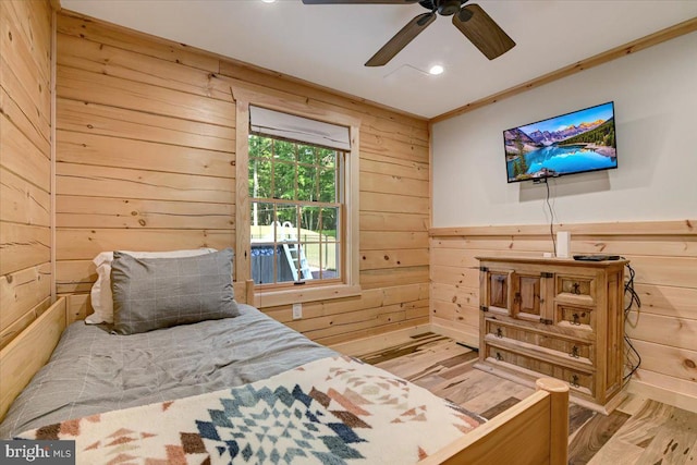 bedroom with light hardwood / wood-style floors, ceiling fan, wood walls, and crown molding