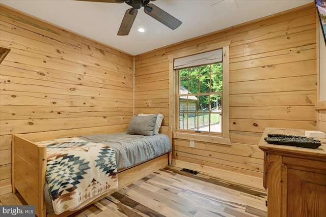 bedroom featuring wood walls, multiple windows, ceiling fan, and light wood-type flooring