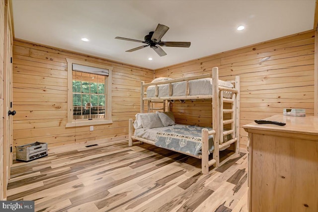 bedroom featuring ceiling fan, wooden walls, and light hardwood / wood-style flooring