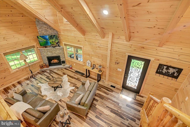 unfurnished living room featuring lofted ceiling with beams, wood ceiling, a stone fireplace, wood walls, and hardwood / wood-style flooring