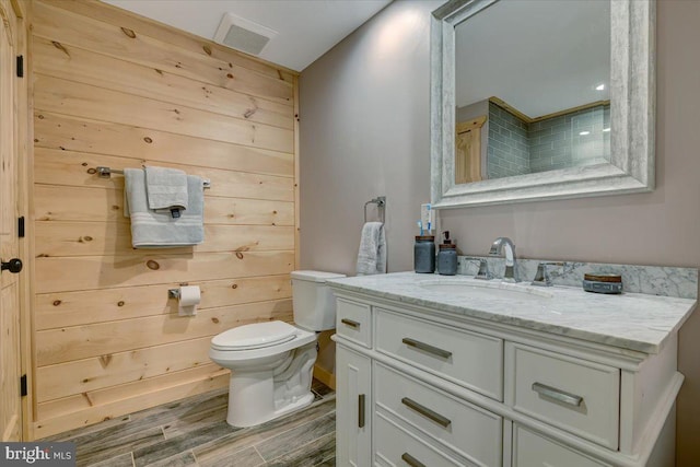 bathroom with vanity, wooden walls, hardwood / wood-style flooring, and toilet