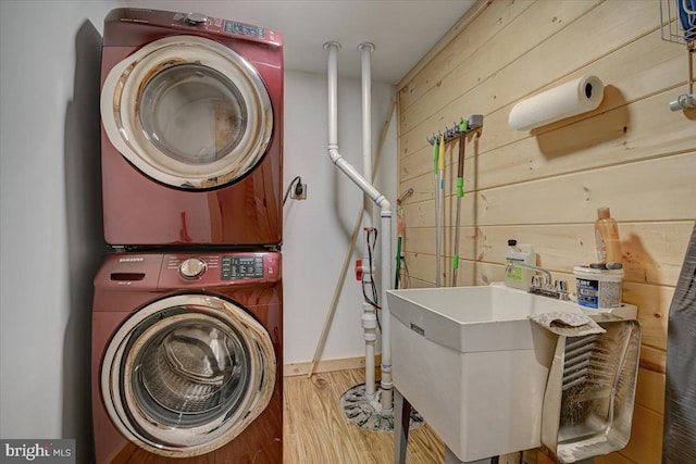 washroom with hardwood / wood-style floors, sink, wooden walls, and stacked washing maching and dryer