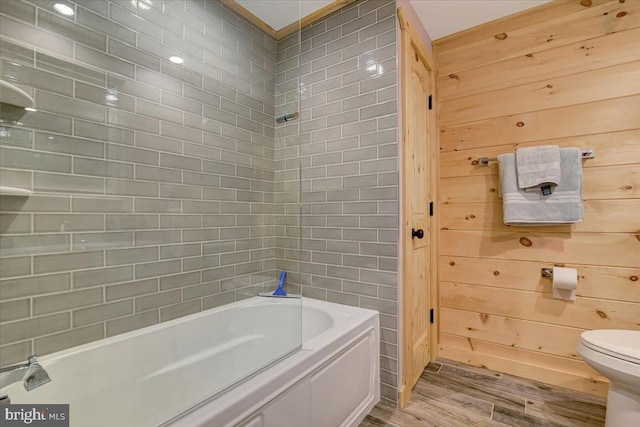 bathroom featuring toilet, wood walls, hardwood / wood-style floors, and tiled shower / bath