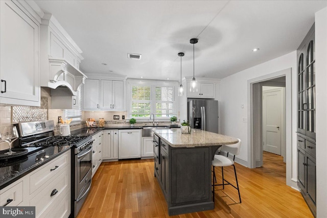 kitchen featuring stainless steel appliances, white cabinetry, a kitchen island, and pendant lighting