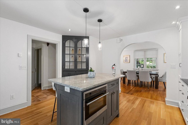 kitchen with pendant lighting, light hardwood / wood-style floors, light stone countertops, a kitchen island, and oven