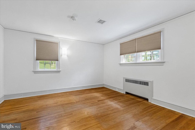 unfurnished room featuring hardwood / wood-style floors, a healthy amount of sunlight, and radiator heating unit