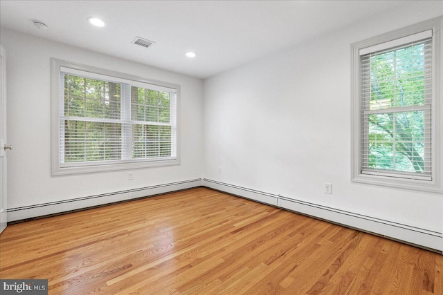 unfurnished room featuring a wealth of natural light, baseboard heating, and light wood-type flooring