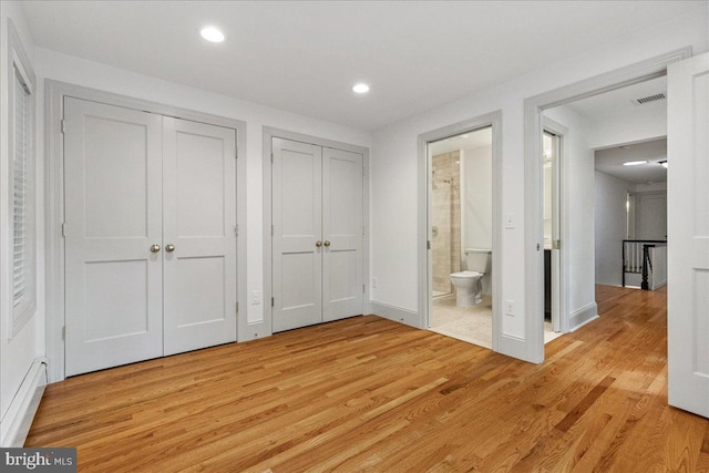 unfurnished bedroom featuring connected bathroom, two closets, and light hardwood / wood-style flooring