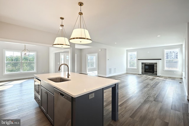 kitchen featuring a stone fireplace, sink, hanging light fixtures, stainless steel appliances, and a kitchen island with sink