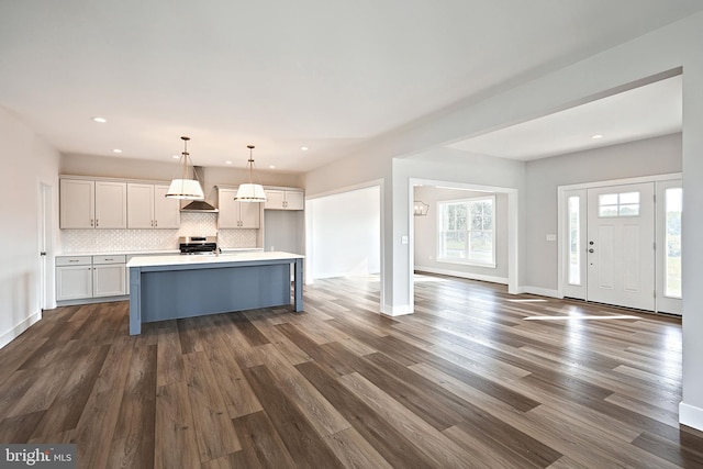 kitchen with stainless steel range oven, a center island with sink, dark hardwood / wood-style flooring, pendant lighting, and decorative backsplash