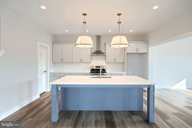 kitchen featuring tasteful backsplash, wall chimney range hood, hanging light fixtures, and a center island with sink