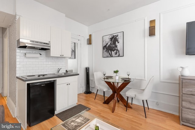 kitchen with under cabinet range hood, a sink, light wood-style floors, black dishwasher, and white cabinets