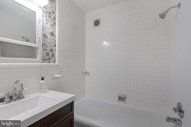 bathroom with backsplash, tile walls, tiled shower / bath combo, and vanity