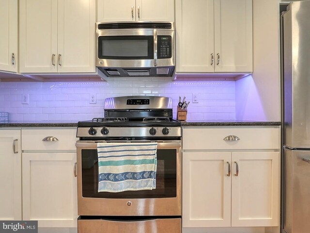 kitchen with decorative backsplash, stainless steel appliances, dark stone countertops, and white cabinets