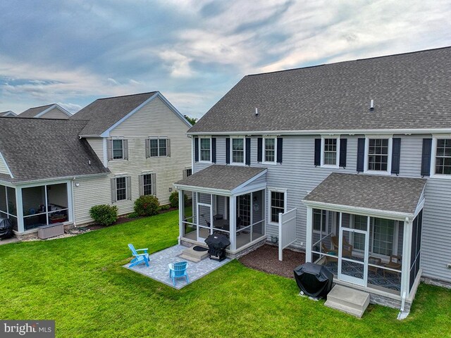 back of property with a sunroom, a lawn, and a patio area