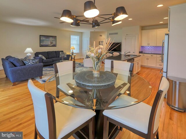 dining room with an inviting chandelier, sink, and light hardwood / wood-style flooring