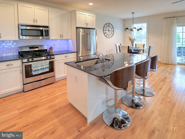 kitchen with white cabinetry, light hardwood / wood-style flooring, backsplash, appliances with stainless steel finishes, and pendant lighting