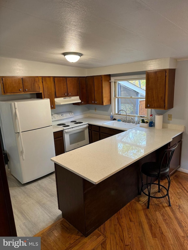 kitchen with light hardwood / wood-style floors, white appliances, kitchen peninsula, and sink