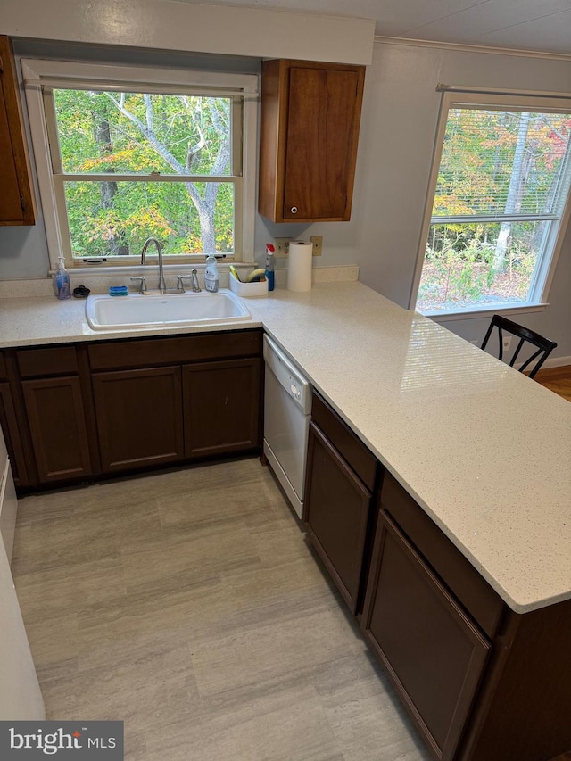 kitchen with light stone counters, white dishwasher, kitchen peninsula, and sink