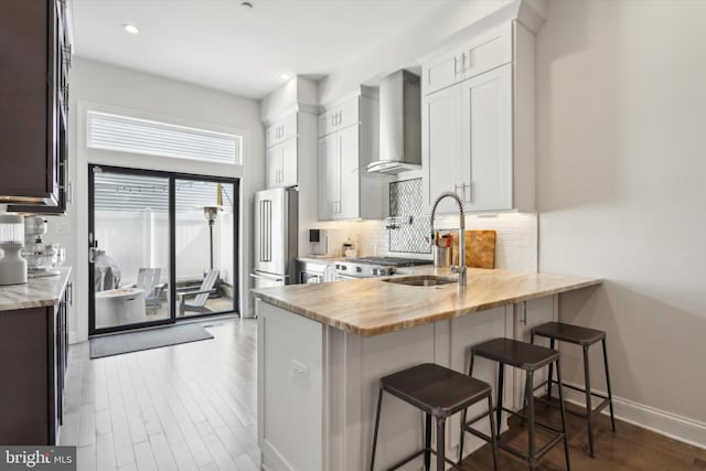 kitchen featuring kitchen peninsula, sink, dark hardwood / wood-style floors, wall chimney exhaust hood, and a breakfast bar area