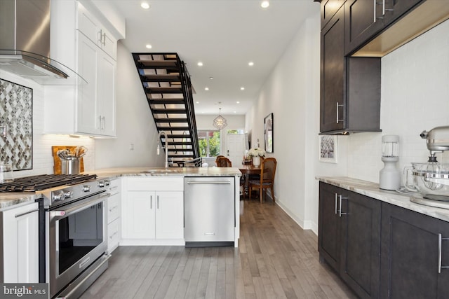 kitchen featuring stainless steel appliances, light stone countertops, wall chimney range hood, and hardwood / wood-style flooring