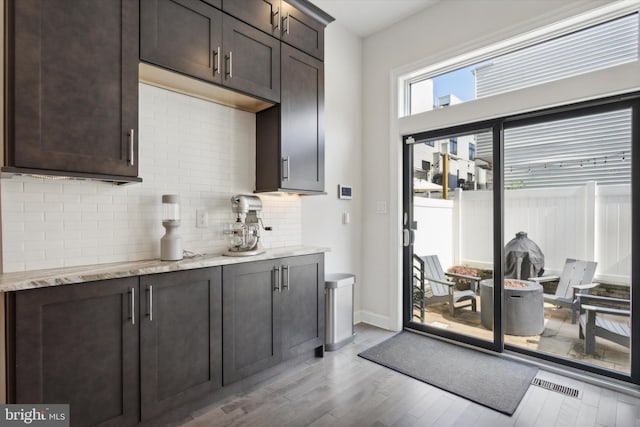 kitchen with backsplash, light stone counters, dark brown cabinets, and light hardwood / wood-style floors