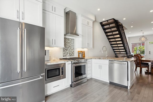 kitchen with wall chimney range hood, wood-type flooring, kitchen peninsula, and premium appliances