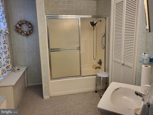 bathroom featuring tile patterned flooring, combined bath / shower with glass door, sink, and tile walls