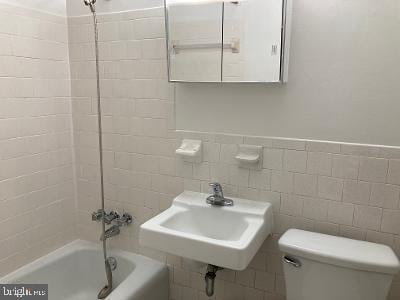 full bathroom with tiled shower / bath, sink, tile walls, and toilet