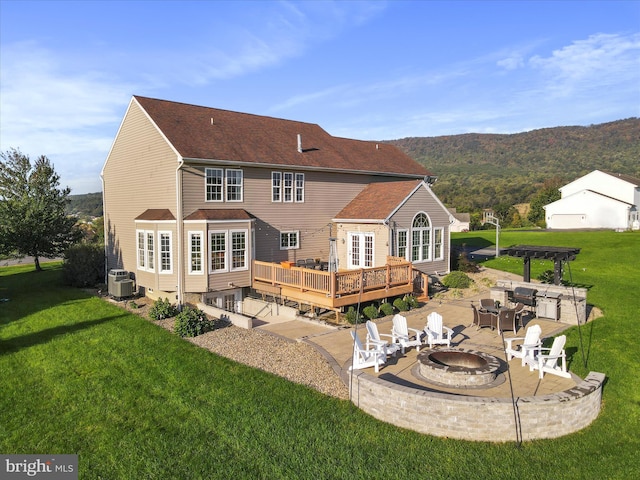 rear view of house with an outdoor fire pit, central AC, a yard, and a deck with mountain view