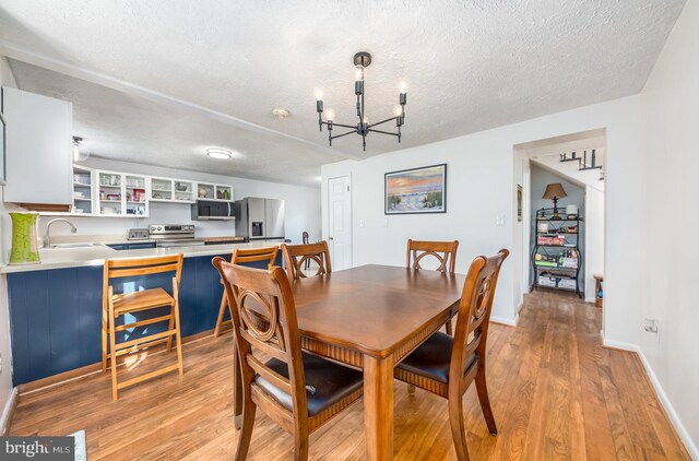 dining area with light hardwood / wood-style floors, sink, a textured ceiling, and a chandelier