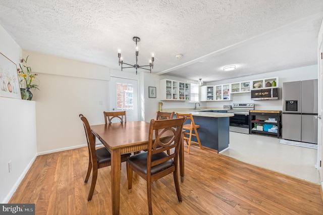 dining space with sink, a chandelier, a textured ceiling, and light hardwood / wood-style floors