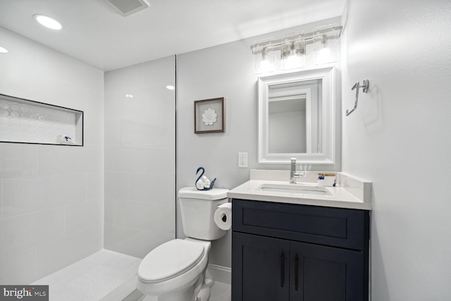 bathroom with tiled shower, vanity, and toilet