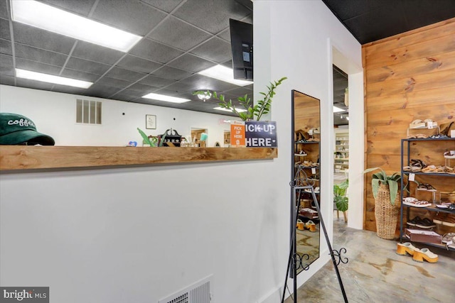 interior space featuring concrete flooring, a paneled ceiling, and wooden walls