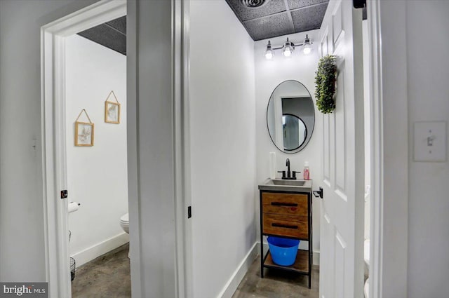 bathroom featuring vanity, concrete floors, toilet, and a drop ceiling