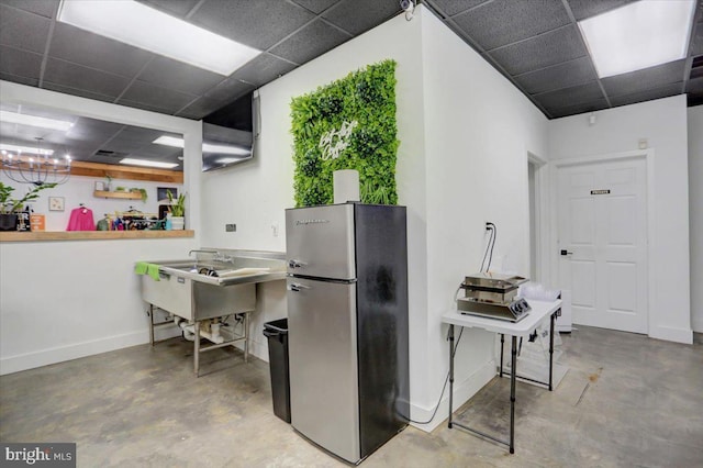 kitchen featuring concrete flooring, sink, a paneled ceiling, and stainless steel fridge