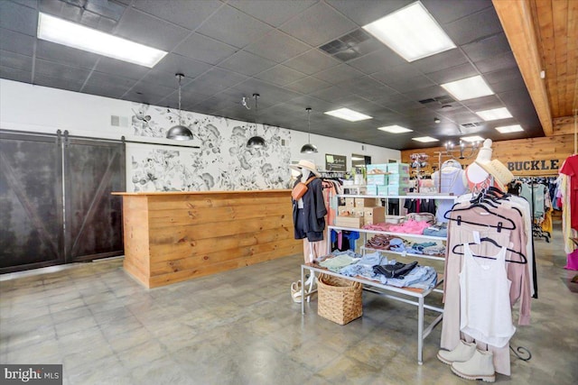 misc room with a paneled ceiling, concrete flooring, wooden walls, and a barn door